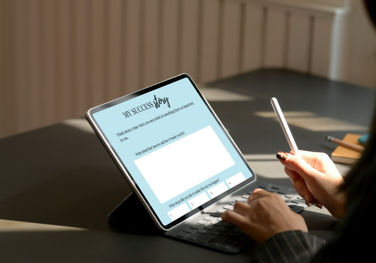 Lady working on her ipad, holding a digital pen, wroting on one of the worksheets. 